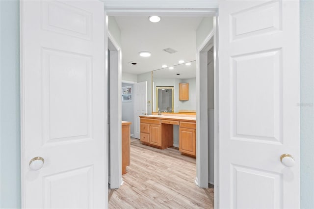 hallway with recessed lighting, visible vents, light wood finished floors, and a sink