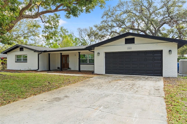 view of front of home featuring driveway, a front lawn, a garage, brick siding, and central AC unit