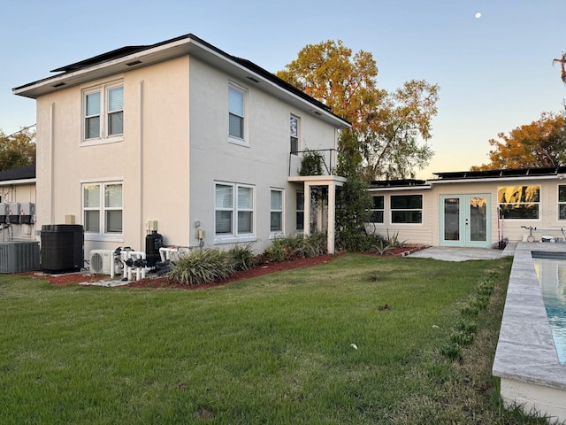 rear view of house featuring french doors, central air condition unit, a yard, and stucco siding