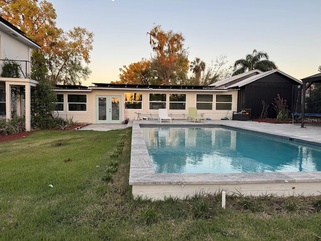 back of property featuring solar panels, a trampoline, a lawn, french doors, and a patio