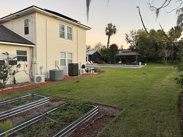 yard at dusk featuring a garden, ac unit, a gazebo, and central AC unit