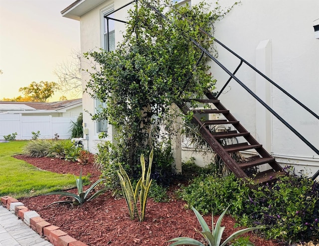 view of property exterior with stairway, fence, a lawn, and stucco siding