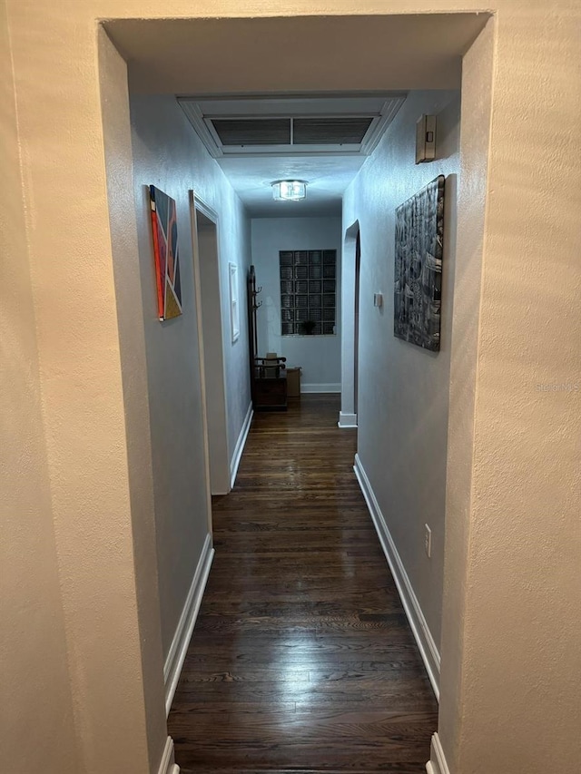 hall featuring a textured wall, baseboards, visible vents, and dark wood-style flooring