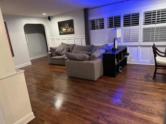 living area with wood finished floors, baseboards, recessed lighting, arched walkways, and a decorative wall