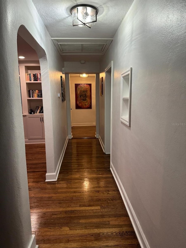 corridor with visible vents, built in shelves, arched walkways, and dark wood-style flooring