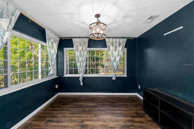 unfurnished dining area with baseboards, visible vents, an inviting chandelier, and wood finished floors