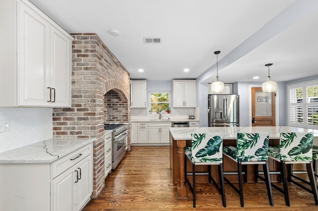 kitchen with a breakfast bar area, stainless steel appliances, visible vents, white cabinets, and wood finished floors