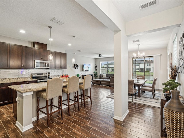 kitchen with wood finish floors, visible vents, a breakfast bar, appliances with stainless steel finishes, and dark brown cabinets