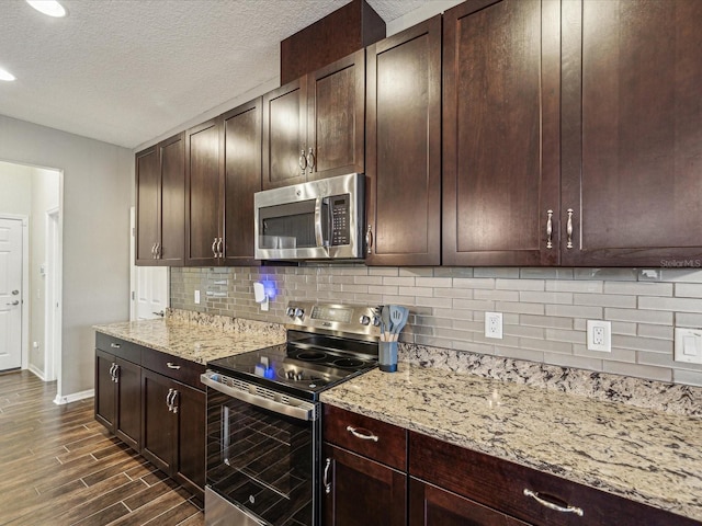 kitchen featuring wood finish floors, dark brown cabinetry, appliances with stainless steel finishes, decorative backsplash, and light stone countertops