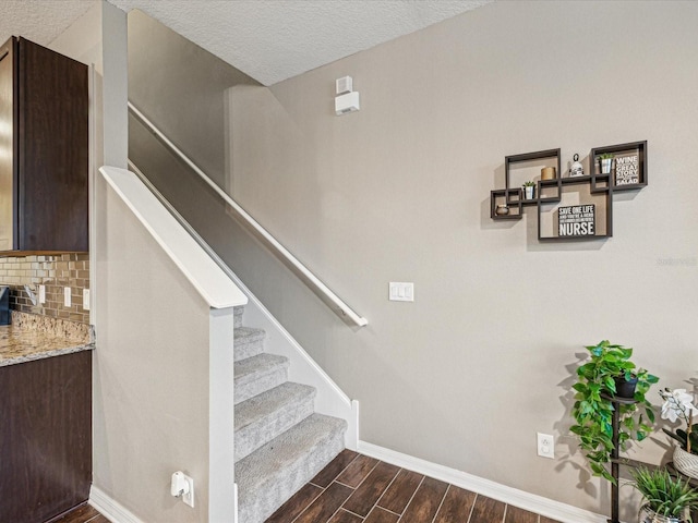 staircase with a textured ceiling, baseboards, and wood finish floors