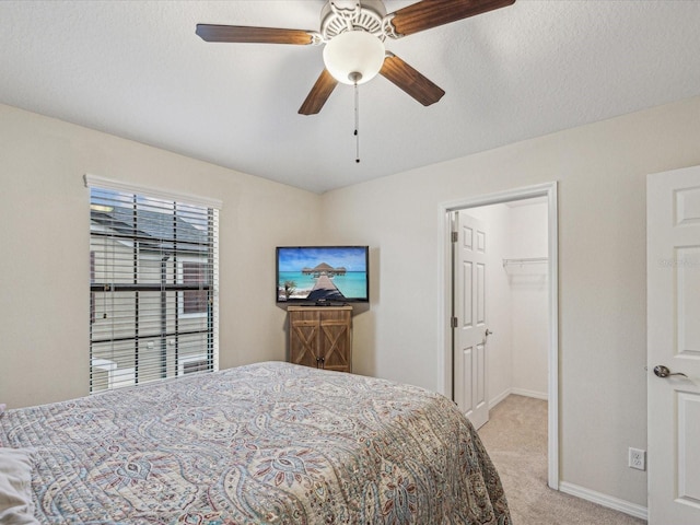 bedroom featuring a walk in closet, a textured ceiling, baseboards, and light carpet