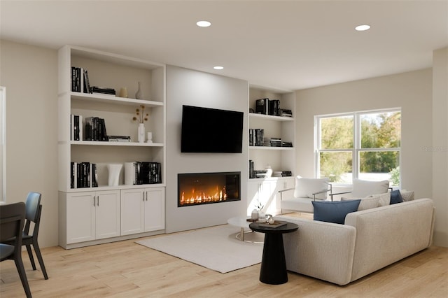 living area with recessed lighting, a lit fireplace, built in features, and light wood-style flooring