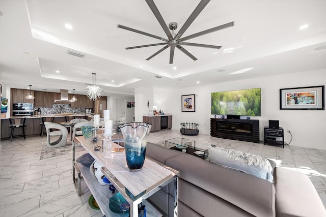 living area featuring visible vents, marble finish floor, ceiling fan with notable chandelier, a tray ceiling, and recessed lighting