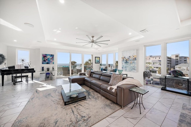 living area with visible vents, a raised ceiling, marble finish floor, and ceiling fan