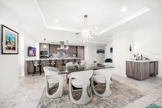 dining room with an inviting chandelier, a raised ceiling, baseboards, and marble finish floor