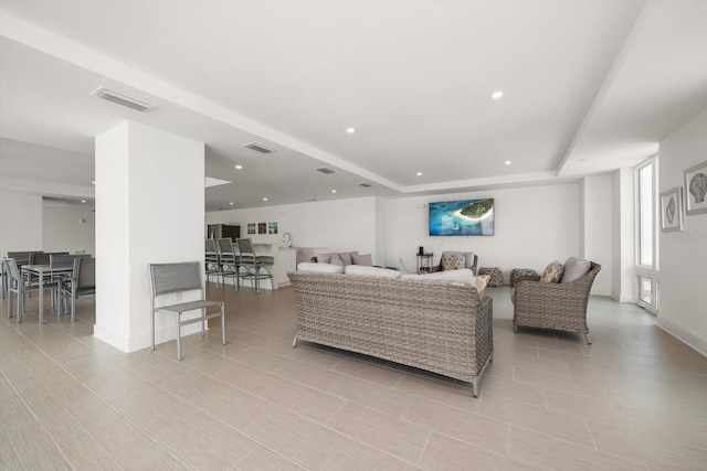 living room featuring recessed lighting, visible vents, a raised ceiling, and baseboards