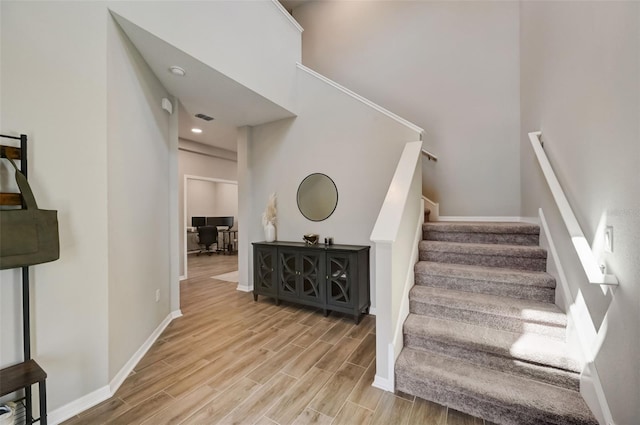 stairway with wood finished floors, baseboards, and a towering ceiling