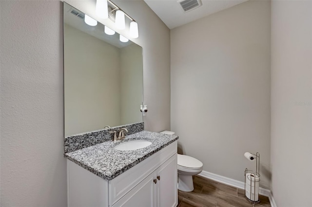 half bathroom featuring vanity, toilet, baseboards, visible vents, and wood finished floors