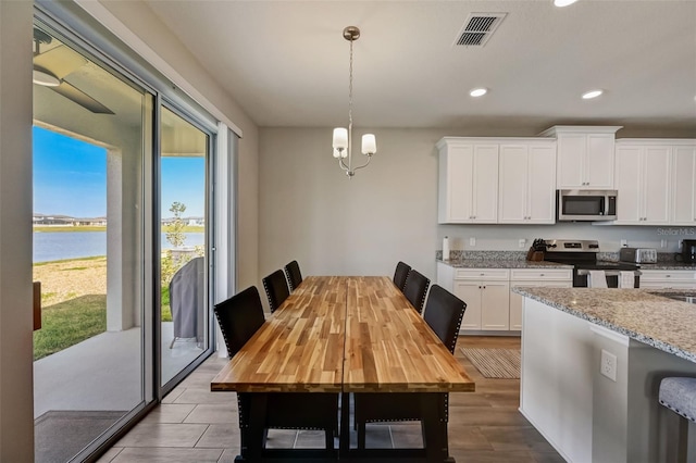 dining area featuring a chandelier, wood finished floors, visible vents, a water view, and recessed lighting
