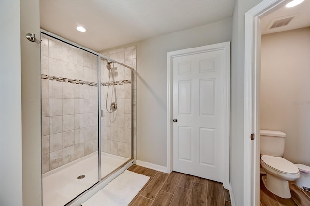 bathroom with toilet, baseboards, a stall shower, visible vents, and wood finished floors