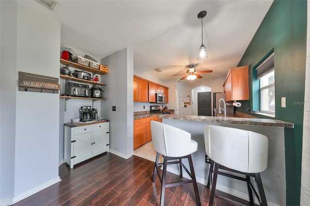 kitchen with ceiling fan, a kitchen bar, a peninsula, dark wood-style floors, and stainless steel appliances