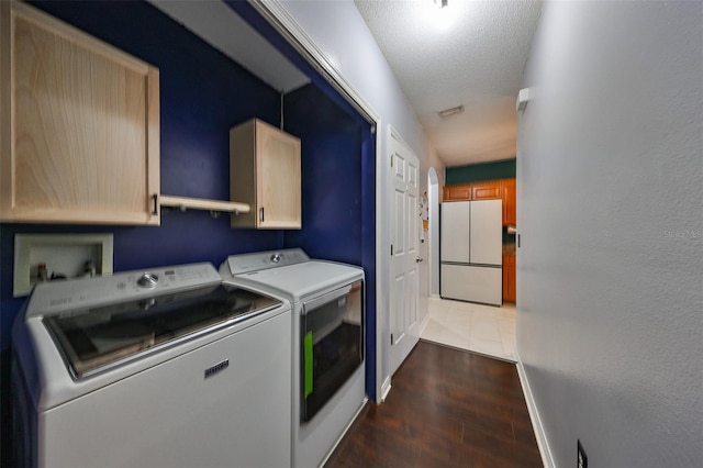 clothes washing area with baseboards, wood finished floors, cabinet space, a textured ceiling, and separate washer and dryer