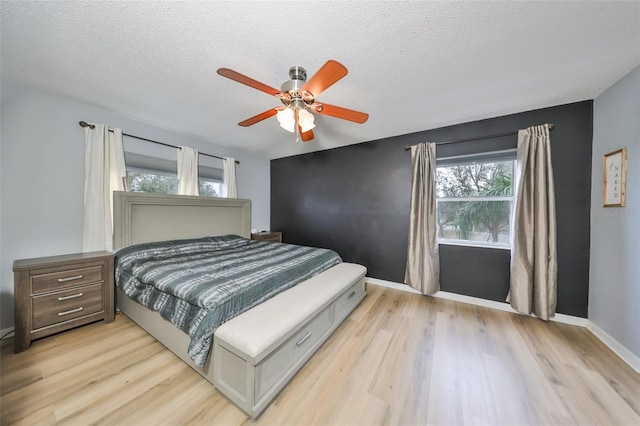 bedroom featuring baseboards, light wood-style floors, a ceiling fan, and a textured ceiling