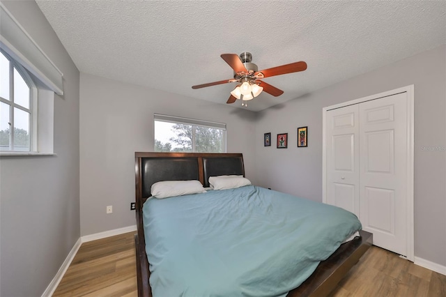 bedroom with baseboards, wood finished floors, a closet, a textured ceiling, and a ceiling fan