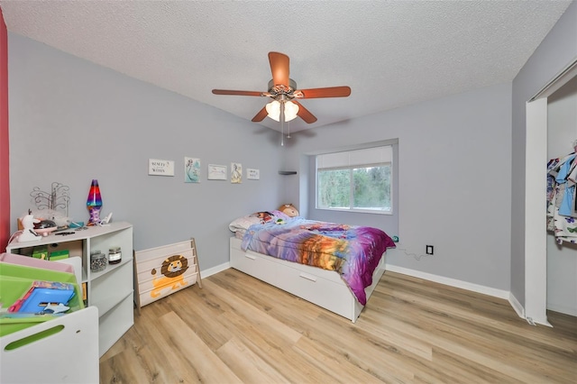 bedroom with a ceiling fan, wood finished floors, baseboards, and a textured ceiling