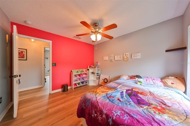 bedroom featuring visible vents, baseboards, light wood-type flooring, a textured ceiling, and a ceiling fan