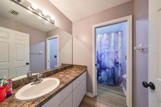 full bathroom featuring visible vents, a shower with curtain, a textured ceiling, wood finished floors, and vanity