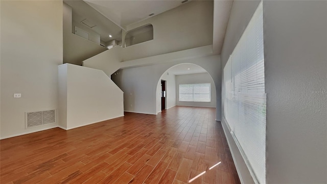 interior space featuring wood finished floors, baseboards, visible vents, arched walkways, and a towering ceiling