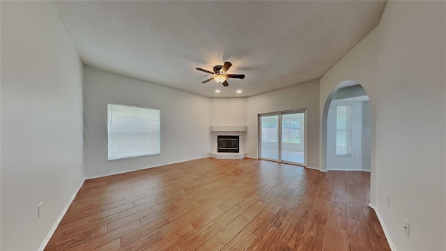 unfurnished living room with a ceiling fan, wood finished floors, baseboards, a textured ceiling, and a tiled fireplace