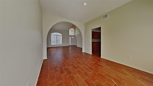 empty room with visible vents, baseboards, dark wood finished floors, lofted ceiling, and arched walkways