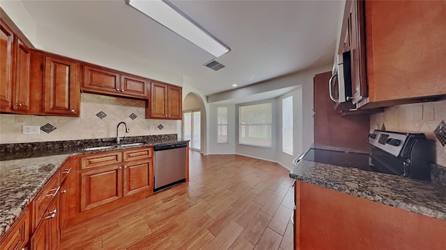 kitchen with dark stone counters, brown cabinetry, appliances with stainless steel finishes, and a sink