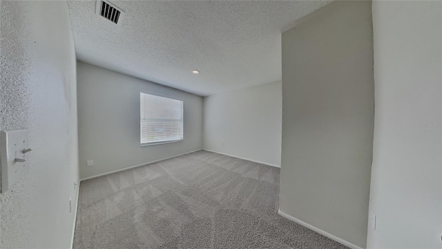 carpeted spare room featuring visible vents, a textured ceiling, and baseboards