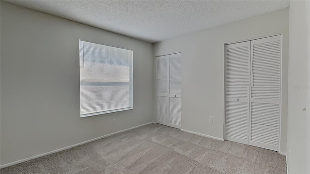 unfurnished bedroom featuring baseboards, multiple closets, a textured ceiling, and light carpet