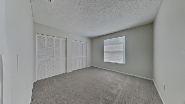 unfurnished bedroom featuring carpet flooring, two closets, a textured ceiling, and baseboards