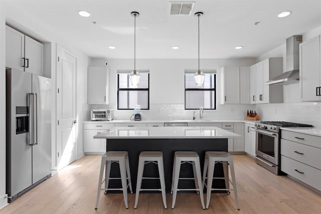 kitchen featuring visible vents, wall chimney range hood, a breakfast bar, high quality appliances, and plenty of natural light