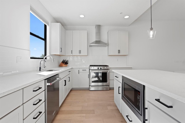 kitchen with a sink, stainless steel appliances, light wood-style floors, wall chimney exhaust hood, and decorative backsplash