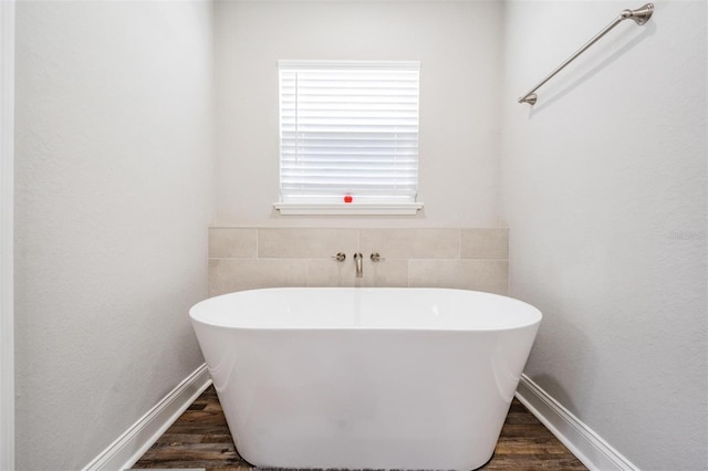 bathroom featuring wood finished floors, baseboards, and a freestanding tub