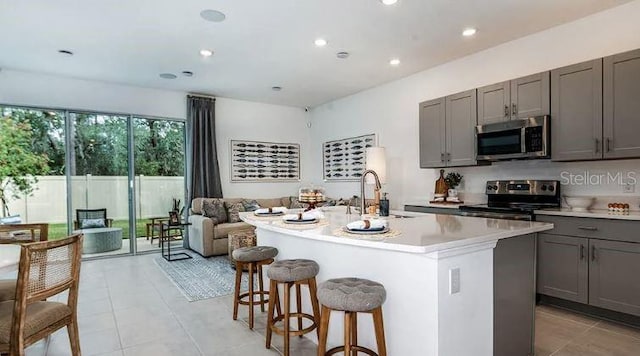 kitchen featuring a kitchen island with sink, a sink, gray cabinetry, light countertops, and stainless steel appliances