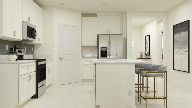 kitchen with light stone countertops, an island with sink, stainless steel appliances, white cabinets, and a kitchen bar