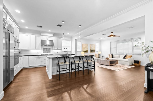 kitchen with under cabinet range hood, open floor plan, a breakfast bar, stovetop, and a sink