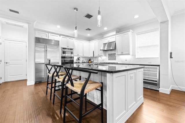 kitchen with dark countertops, visible vents, under cabinet range hood, decorative backsplash, and stainless steel appliances