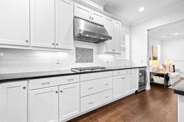 kitchen featuring dark countertops, under cabinet range hood, stainless steel gas cooktop, beverage cooler, and ornamental molding