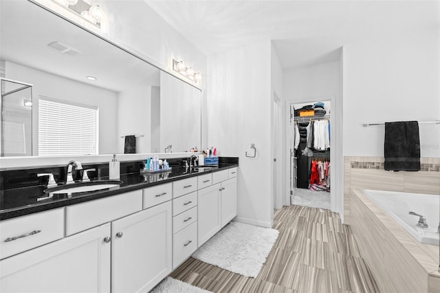 bathroom with visible vents, a walk in closet, a garden tub, a sink, and double vanity