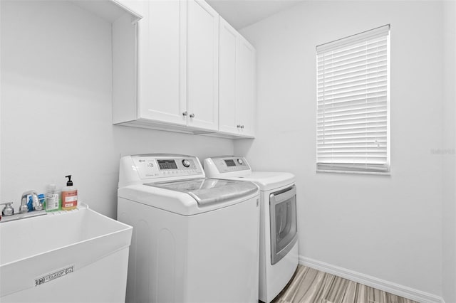 laundry room with a sink, washing machine and dryer, cabinet space, light wood finished floors, and baseboards