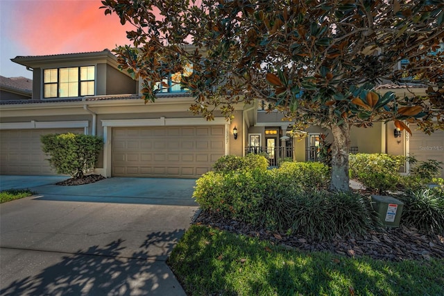 townhome / multi-family property with stucco siding, concrete driveway, an attached garage, and a tile roof