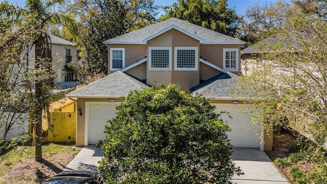 traditional-style home with stucco siding, roof with shingles, concrete driveway, and fence